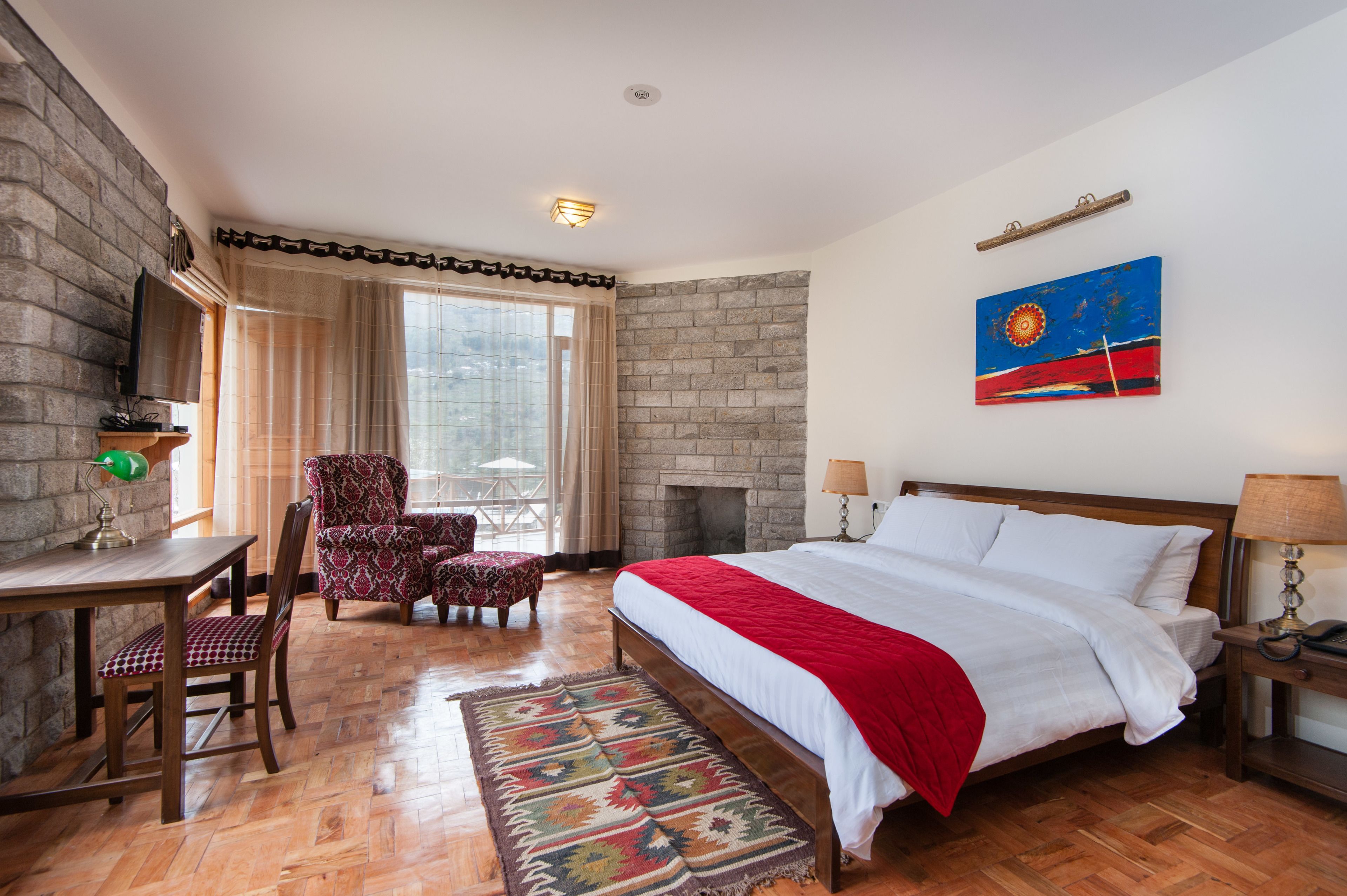 A bedroom with a large bed, a desk, a chair, a fireplace, and a window with curtains.