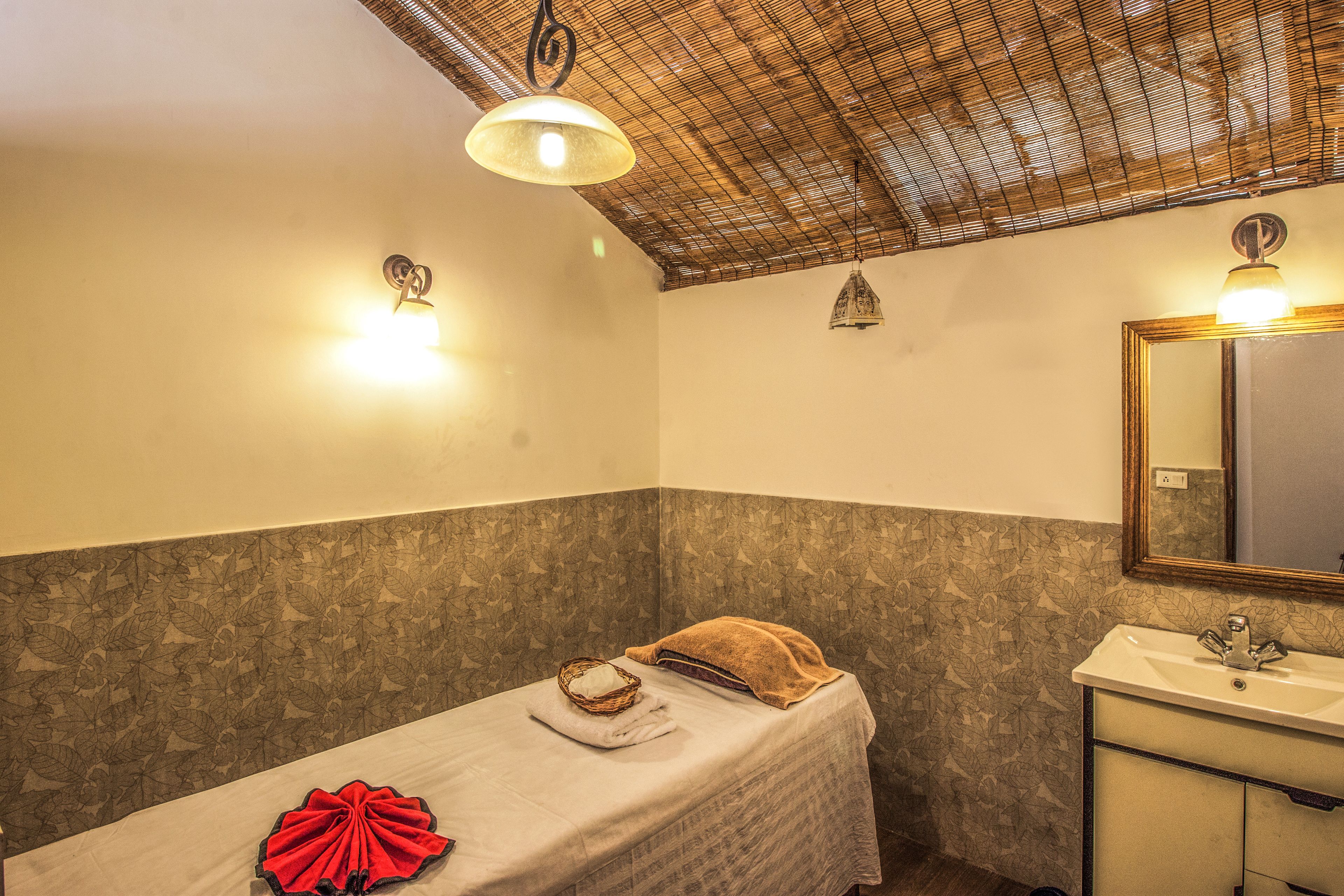 A small, single-bed room with a wooden ceiling, a wall-mounted sink, and a mirror.
