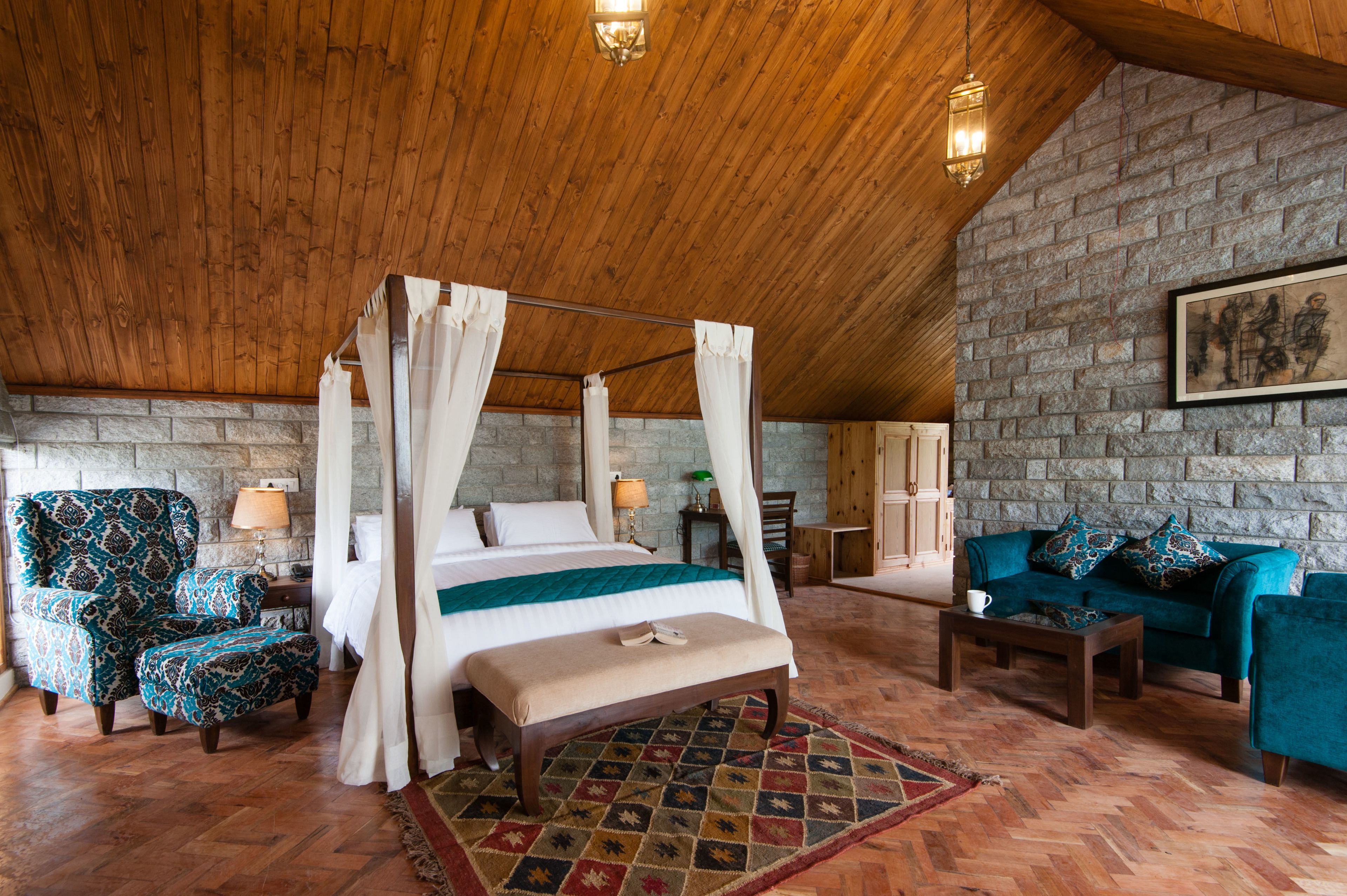 A bedroom with a four-poster bed, a sitting area with a sofa and armchairs, and a stone wall.