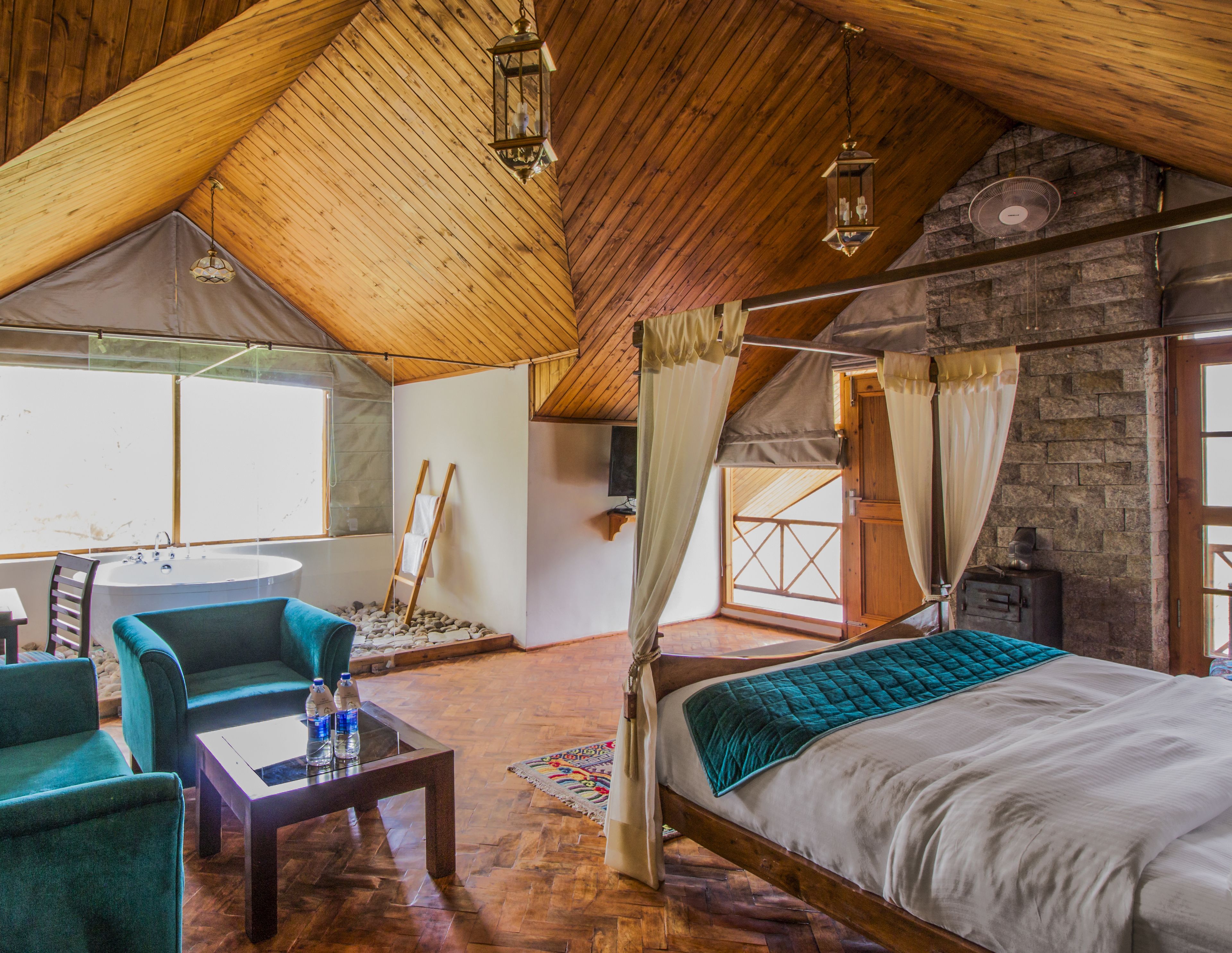 A cozy bedroom with a wooden ceiling, a large bed, a sitting area with chairs, and a view of the outside.
