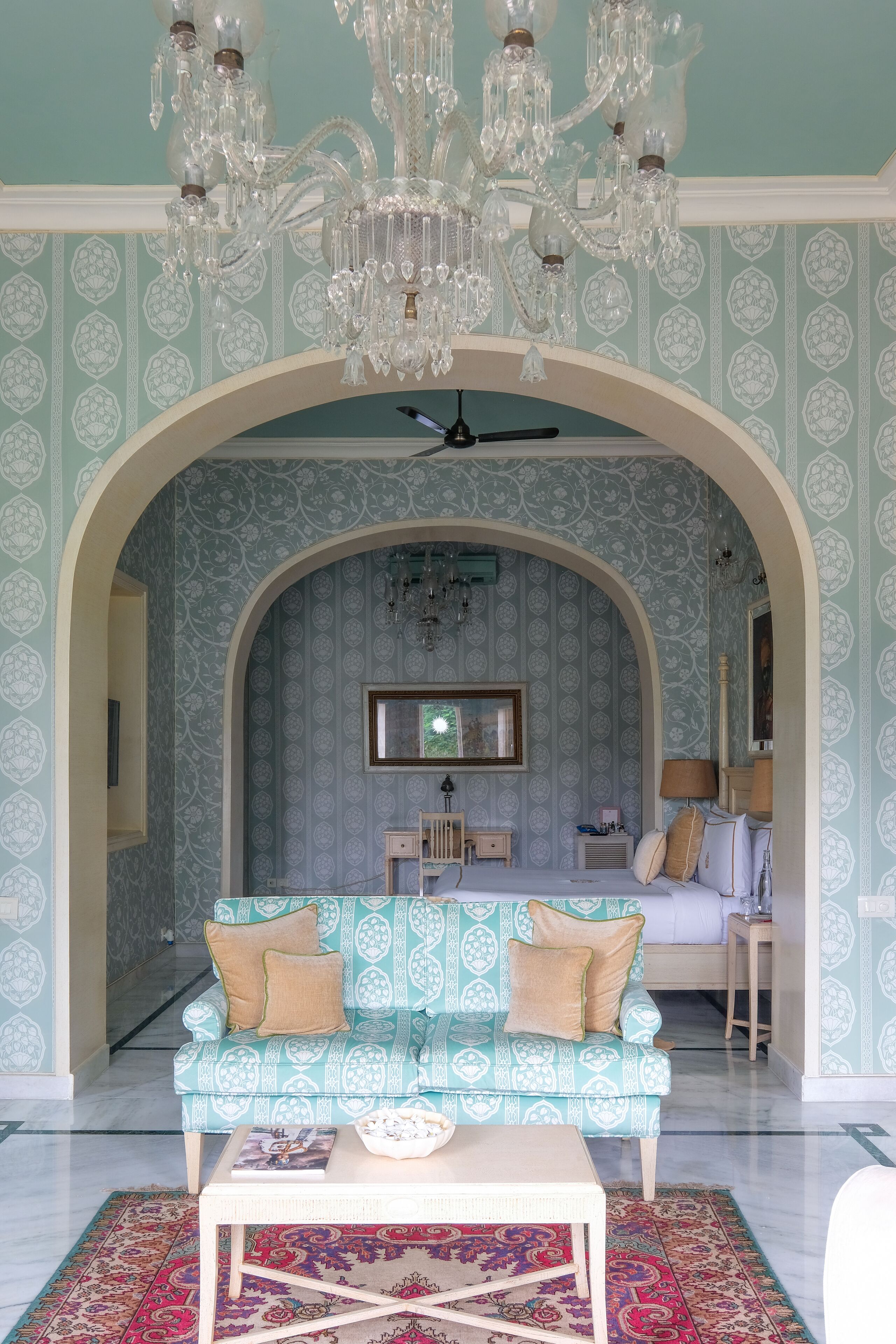 A room with a patterned wallpaper, a chandelier, a sofa, and a coffee table.
