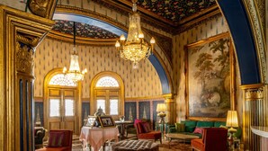 Una habitación opulenta con candelabros ornamentales, un cuadro imponente y muebles clásicos.