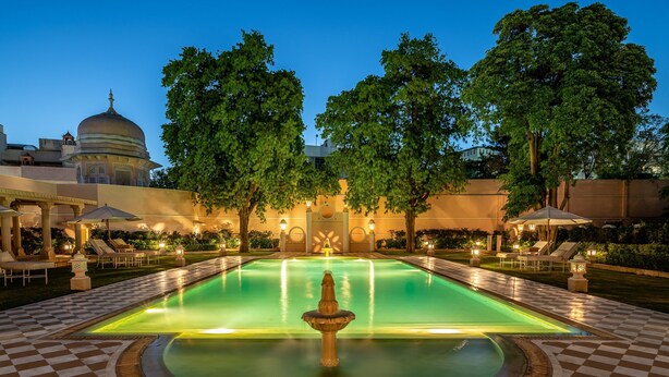 Una piscina con una fuente, rodeada de suelo a cuadros y sillones de descanso.