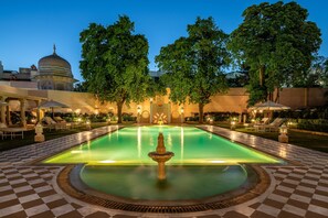 Una piscina con una fuente, rodeada de suelo a cuadros y sillones de descanso.