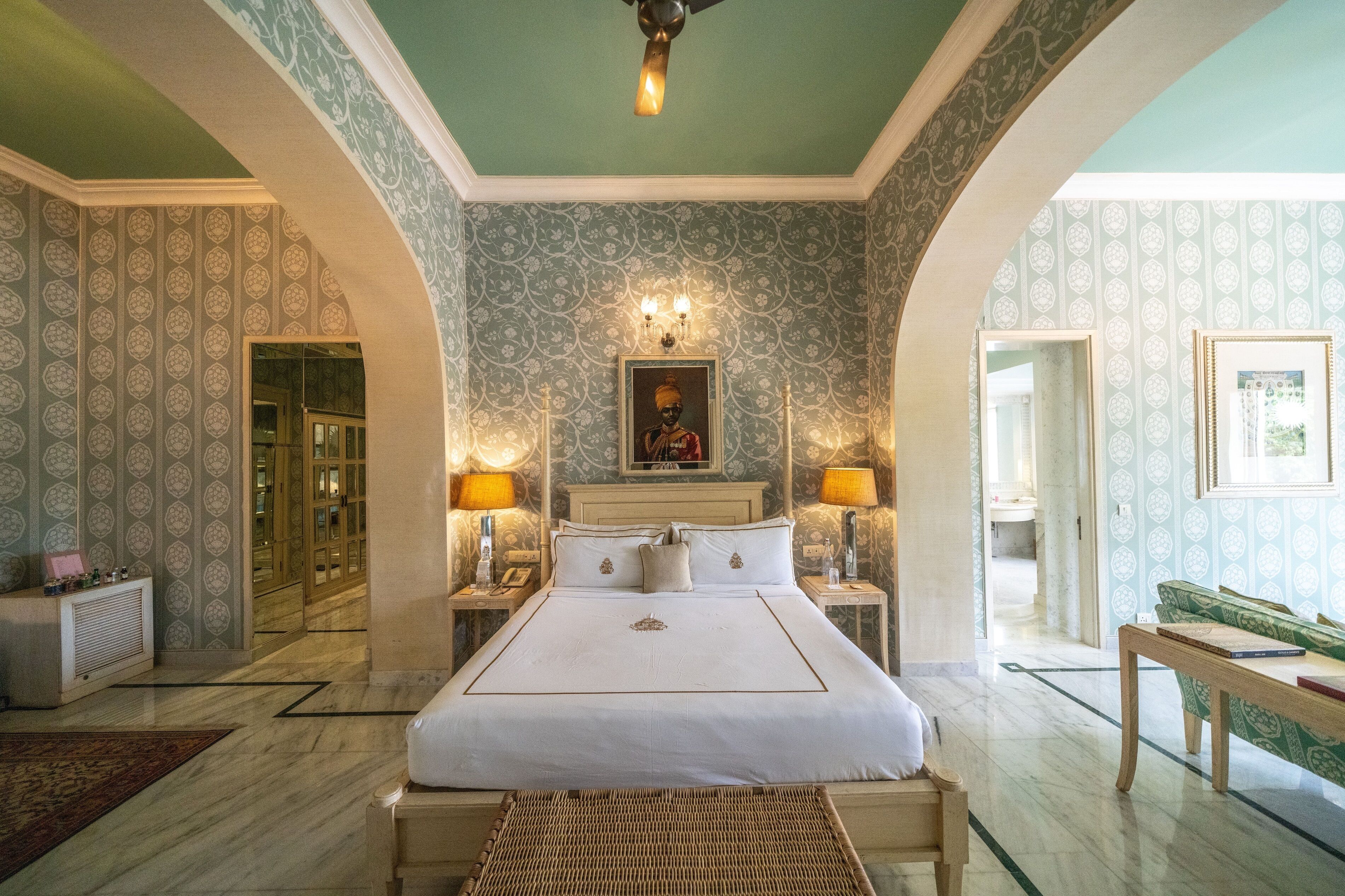 Um quarto espaçoso com uma cama grande, duas mesas de cabeceira com abajures, um criado-mudo e um sofá verde.