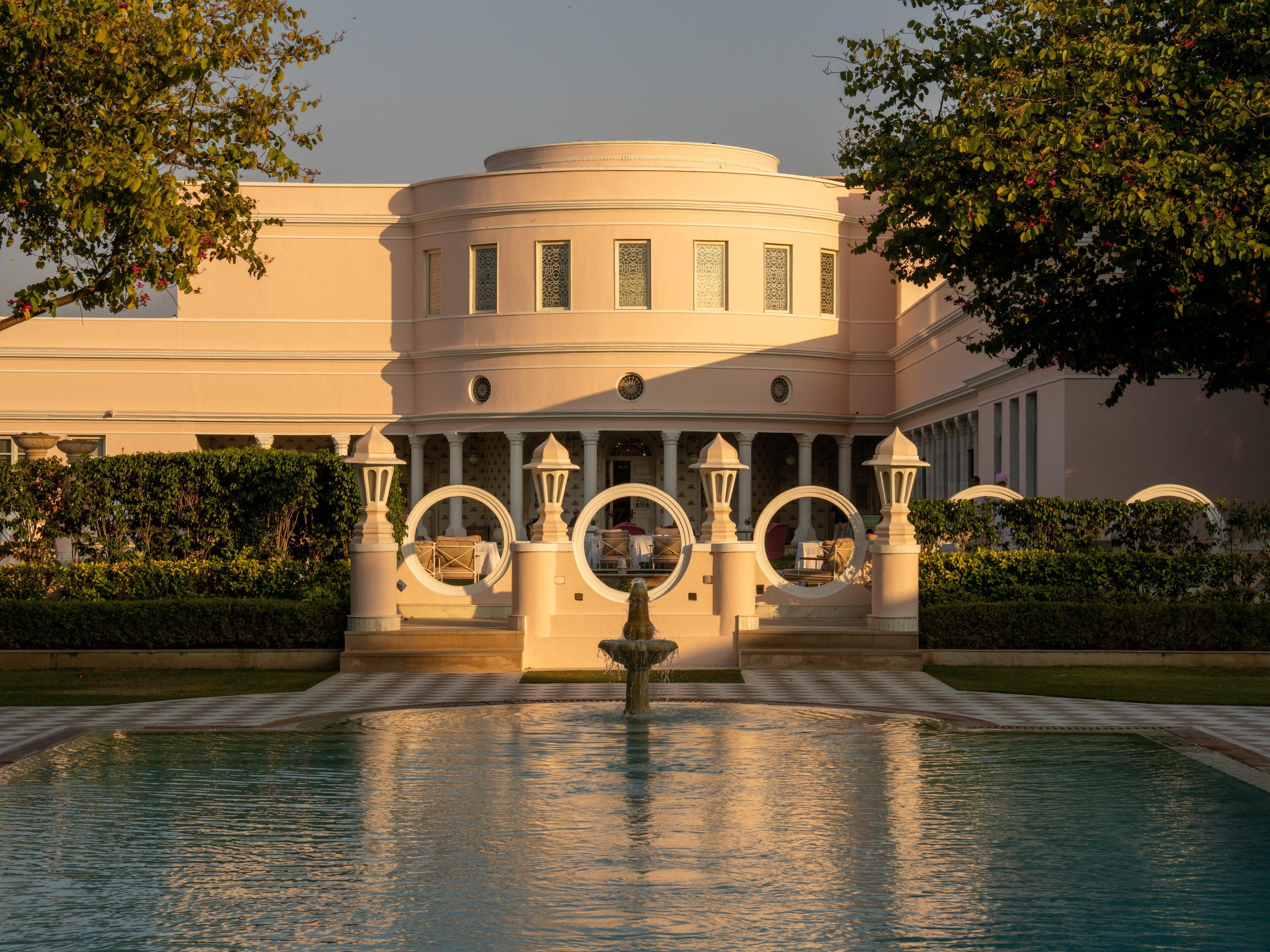 A building with a fountain in front, surrounded by a pool and greenery.