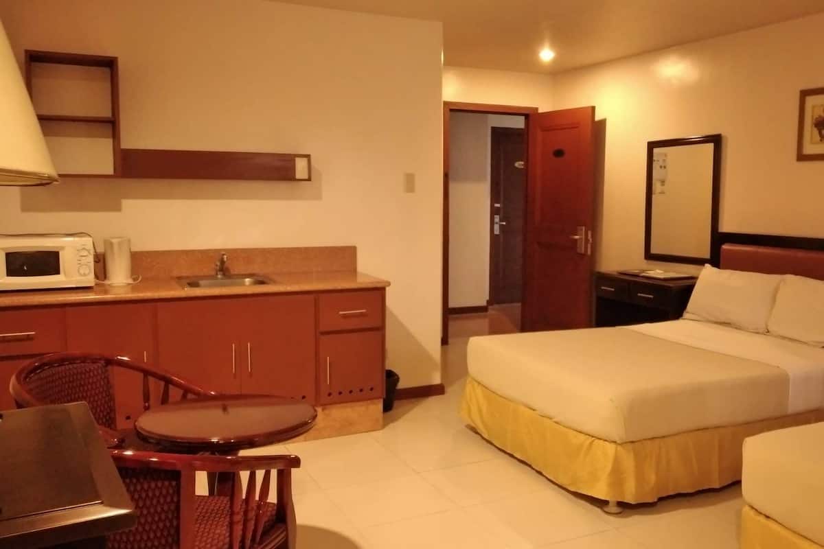 A hotel room with a bed, a desk with a chair, a microwave, and a sink.