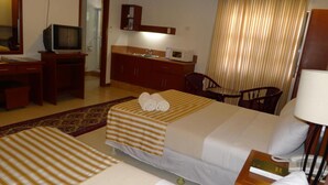 A hotel room with two beds, a desk, a television, a minibar, and a bathroom. - Hotel Cosmopolitan (Baguio)