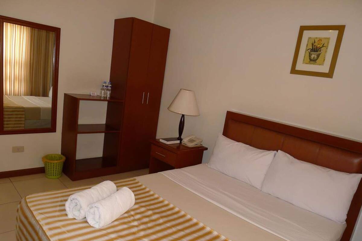 A hotel room with a bed, a nightstand, a lamp, a wardrobe, a mirror, and a framed picture on the wall.