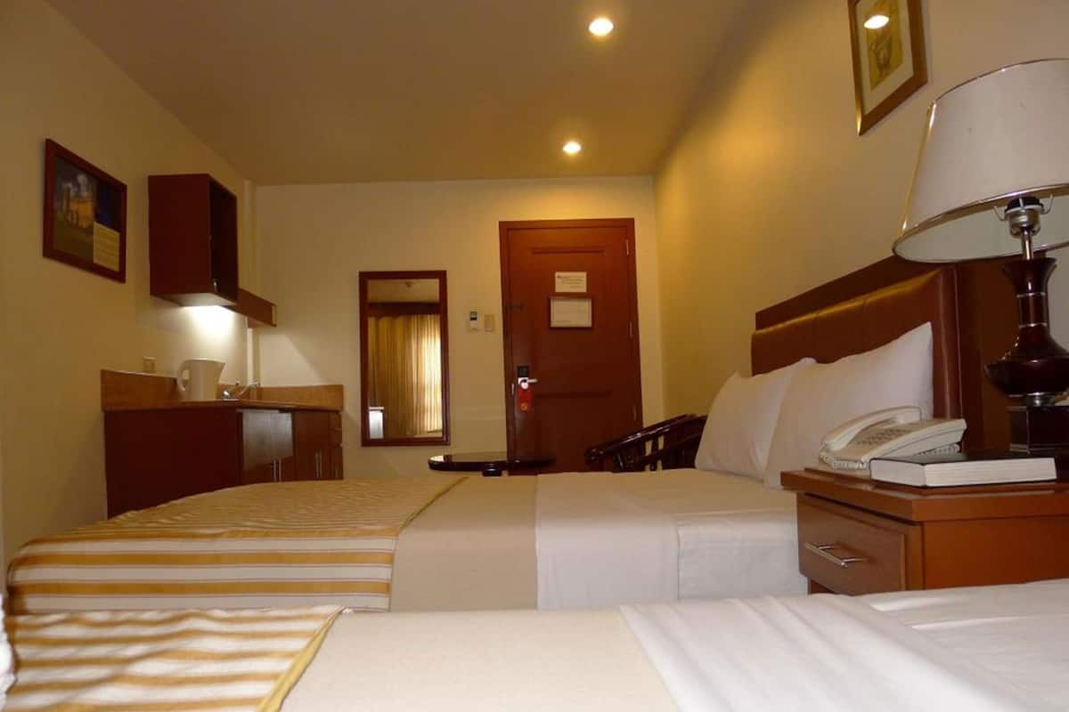 A hotel room with two beds, a desk, a telephone, a lamp, and a mirror.