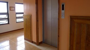A hallway with a wooden door, a metal elevator, and a window with a sign. - Hotel Cosmopolitan (Baguio)