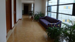 A hallway with a sofa, potted plants, and a large window. - Hotel Cosmopolitan (Baguio)