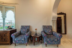 Quarto com duas poltronas florais, uma pequena mesa de madeira com um vaso e um espelho grande.