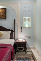 A bedroom with a bed, a bedside table, a nightstand, a wall-mounted light fixture, and a decorative wall panel.