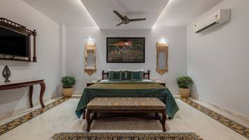 A bedroom with a bed, bench, decorative pillows, wall-mounted lights, a ceiling fan, and a framed painting.