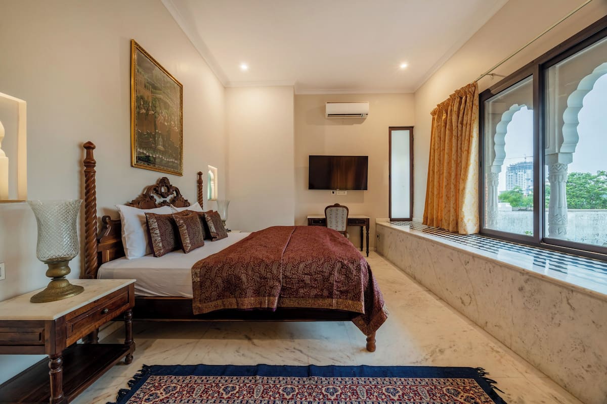 A bedroom with a bed, a nightstand, a lamp, a television, and a window with curtains.