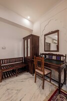 Um quarto com um banco de madeira, uma cadeira, um armário e um espelho na parede.