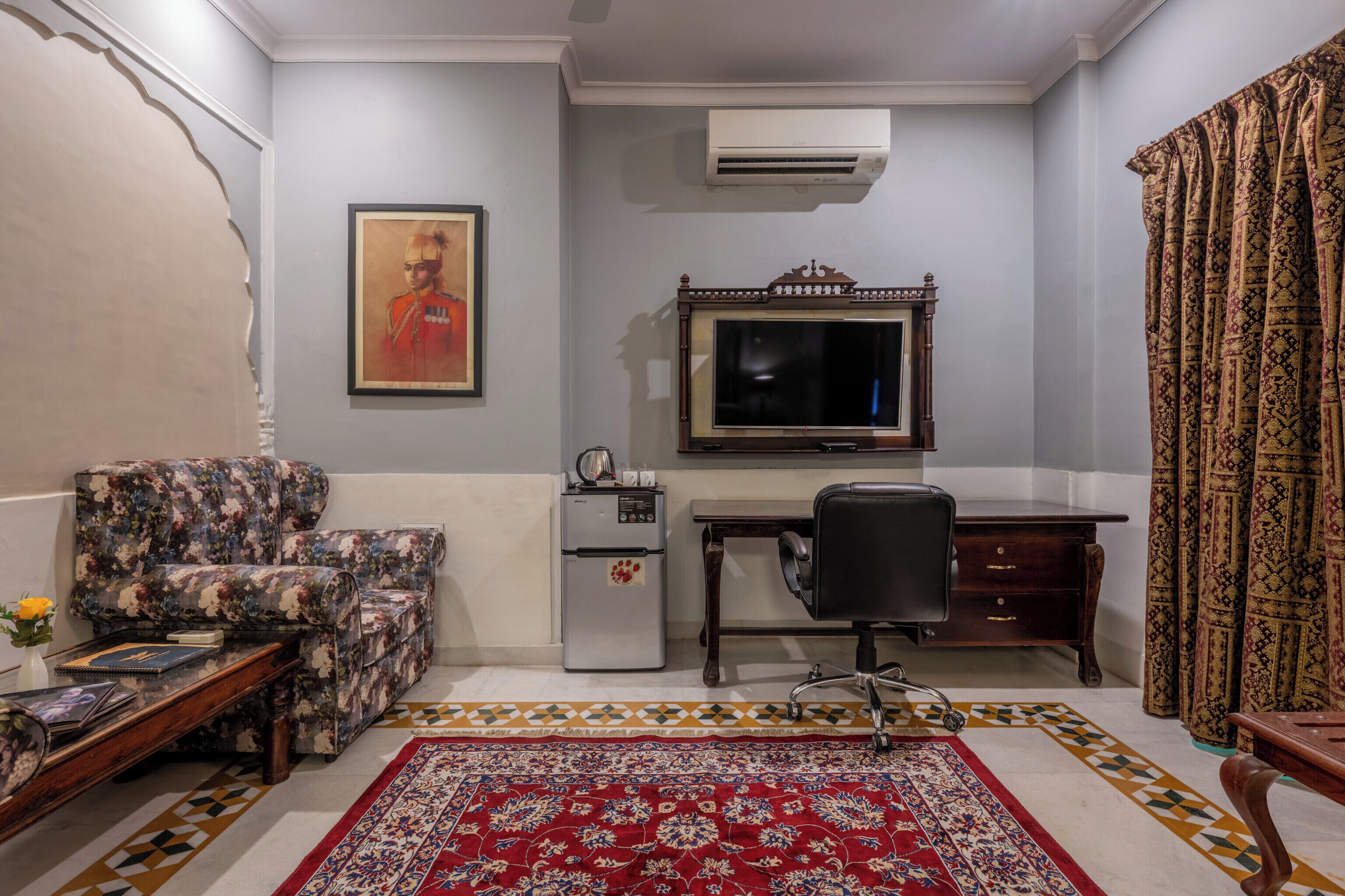 A room with a sofa, a desk, a chair, a refrigerator, an air conditioner, and a patterned rug.