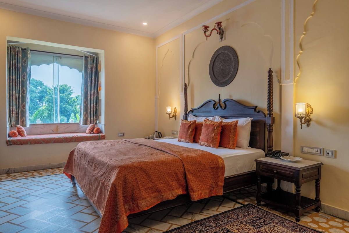 A bedroom with a bed, a nightstand, a window with curtains, and a wall-mounted lamp.