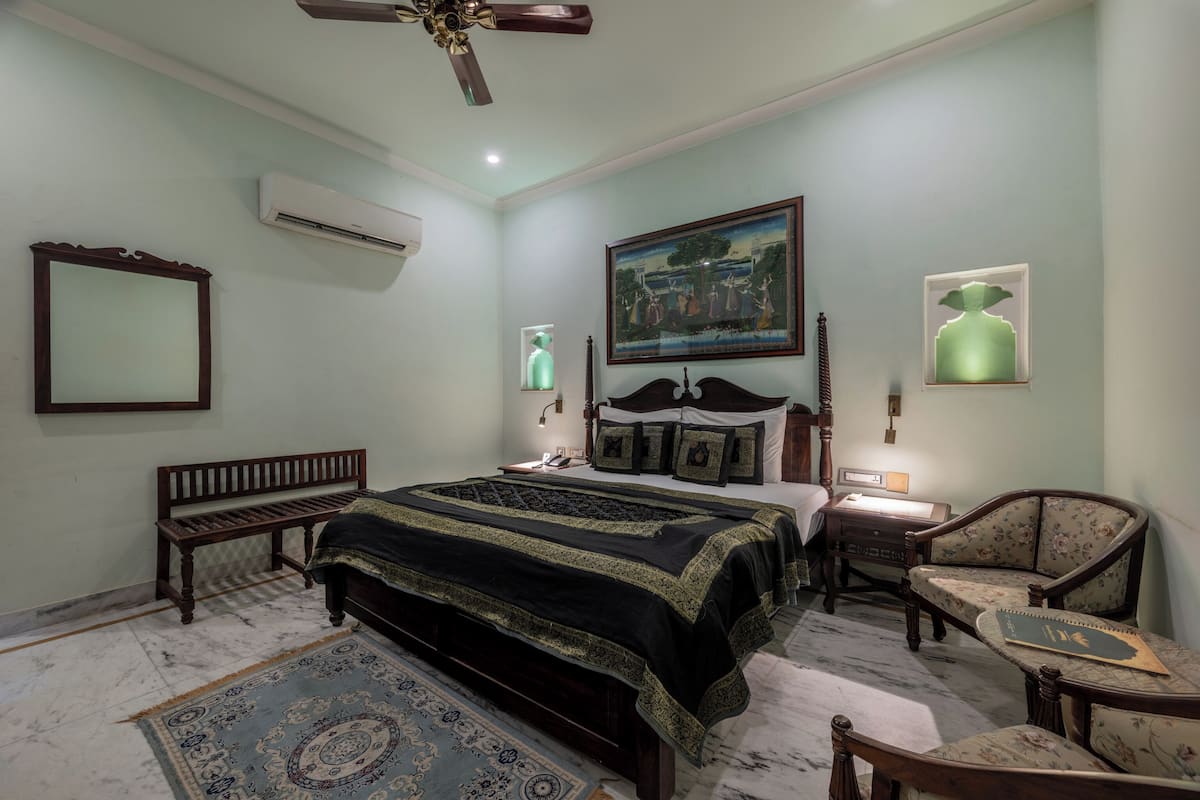 A bedroom with a large bed, a wooden bench, a chair, a desk, and a ceiling fan.
