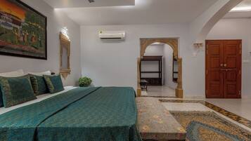 A bedroom with a bed, a painting, an air conditioner, a wooden door, and a patterned rug.