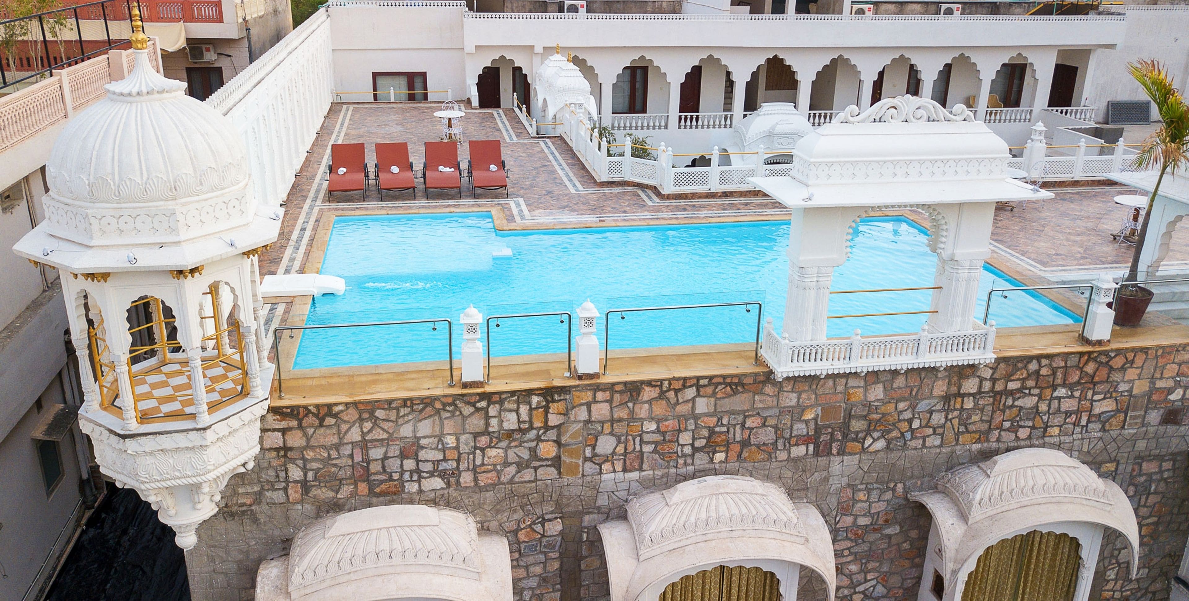 A pool area with stone walls, white architectural details, and red lounge chairs.