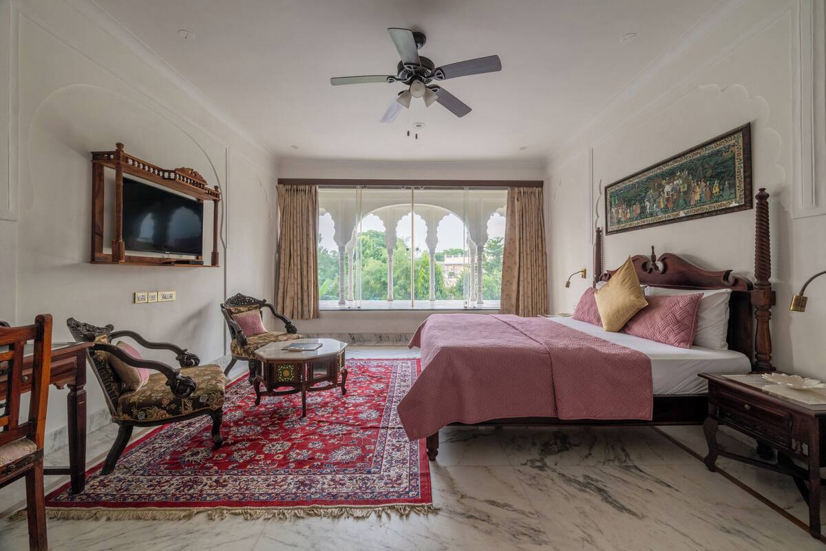 A bedroom with a bed, a ceiling fan, a TV, and a window with curtains.
