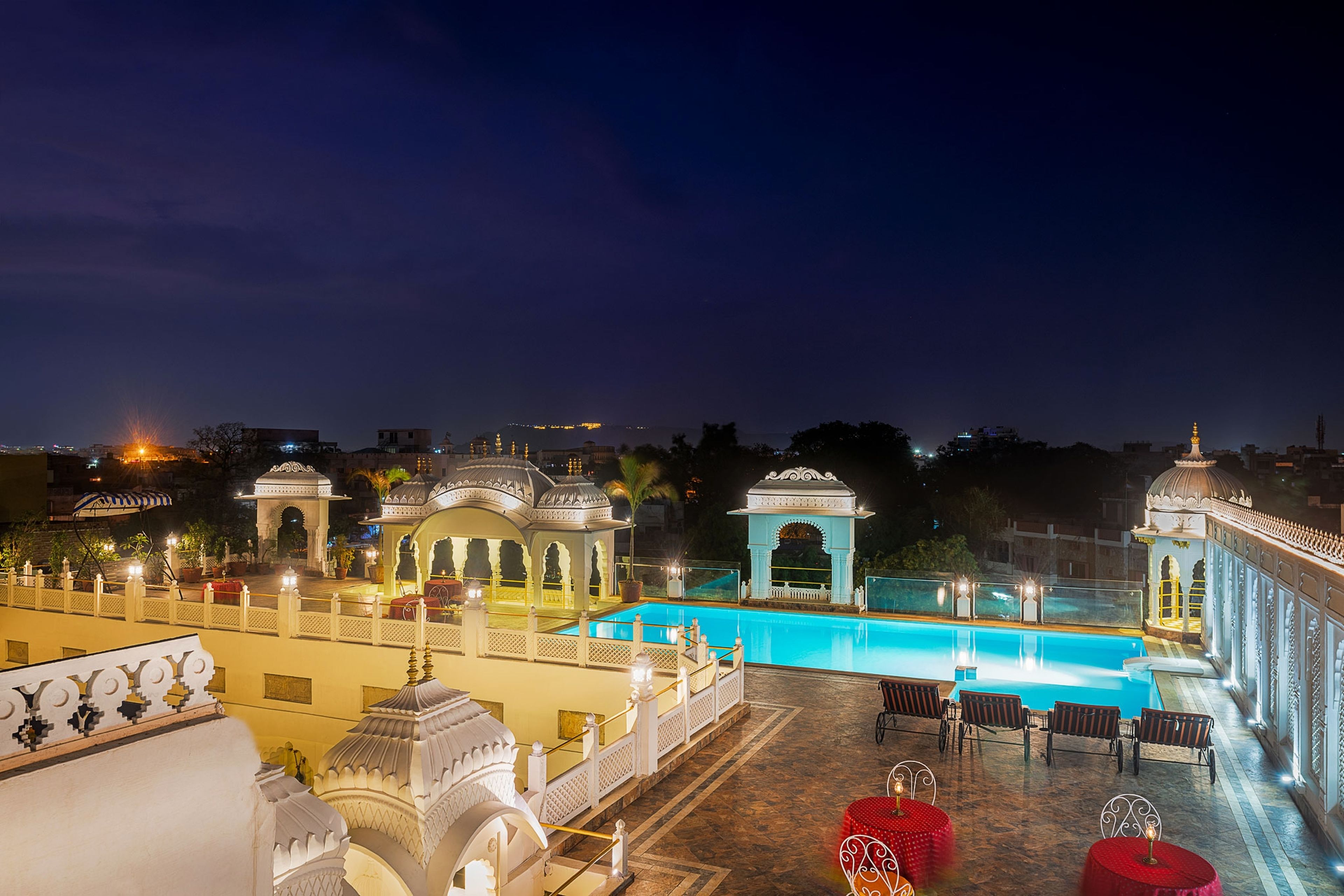 A nighttime view of a hotel with a swimming pool, outdoor seating, and traditional architecture.