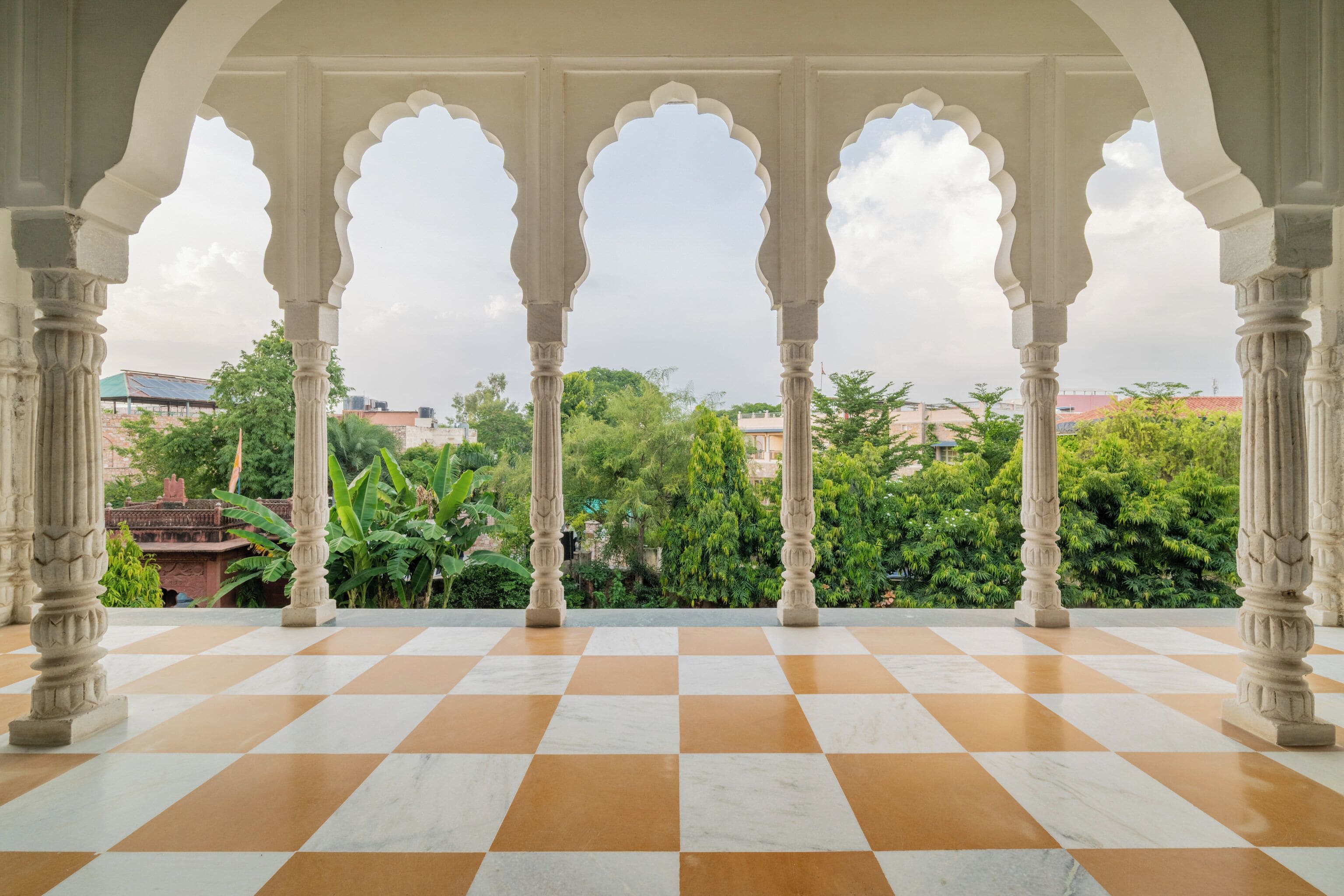 A checkered floor with ornate pillars and a view of greenery and buildings.