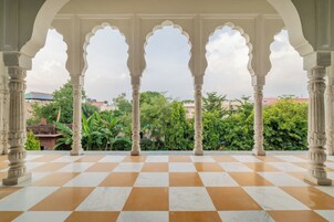 Piso xadrez com pilares ornamentados e vista para áreas verdes e edifícios.