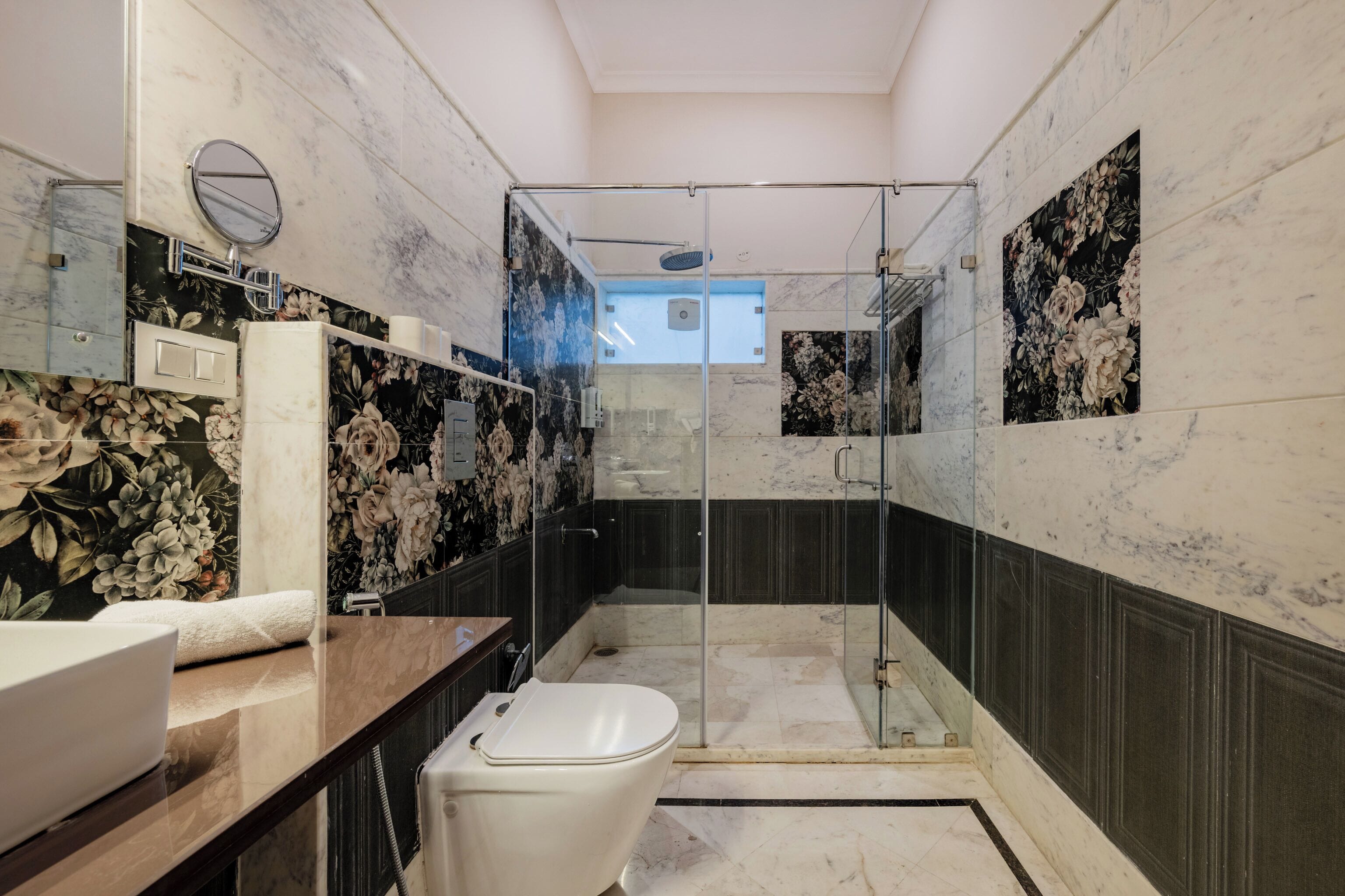 Un baño moderno con ducha envuelta en vidrio, inodoro blanco y tocador con azulejos de mármol.