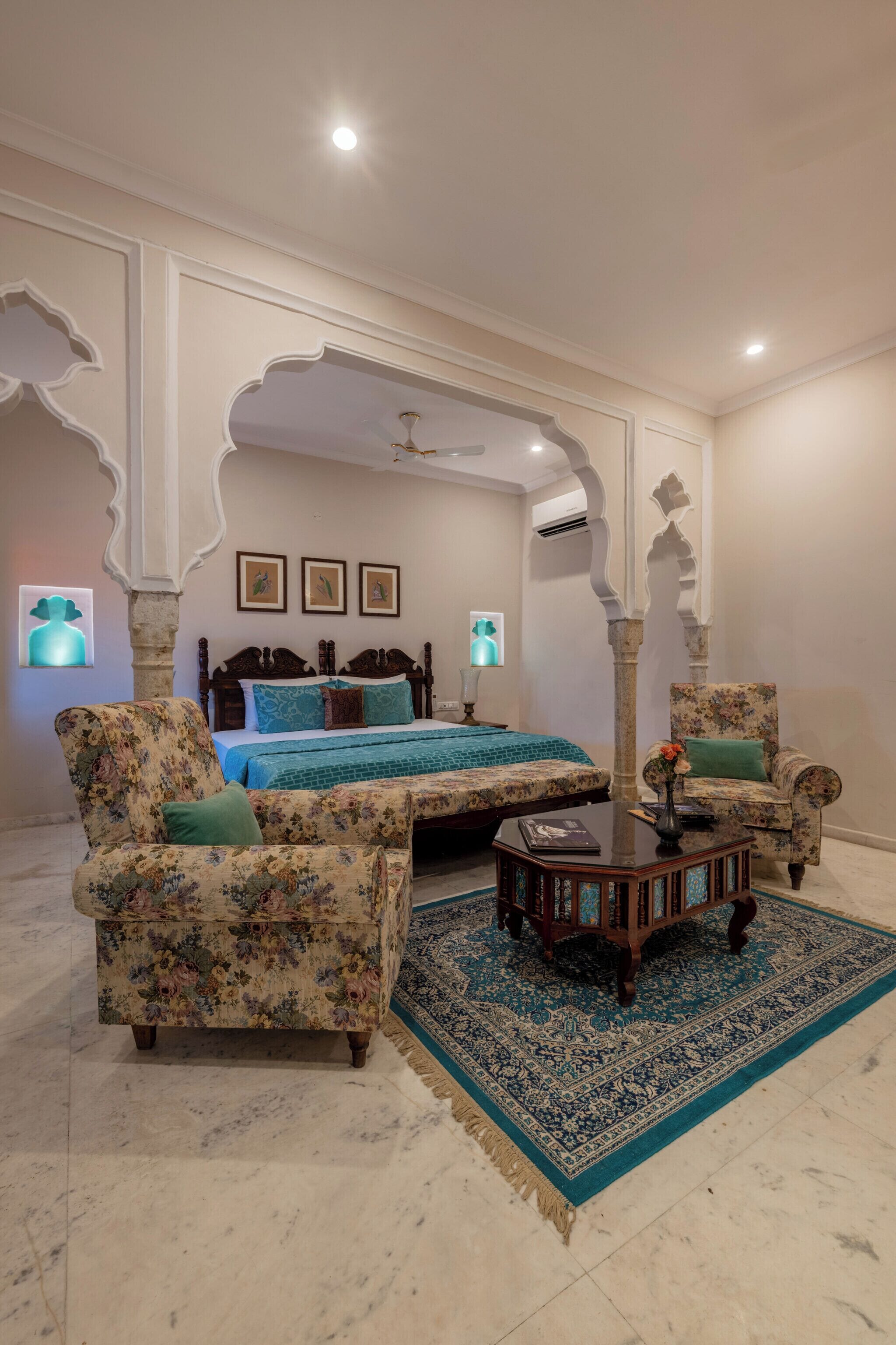 A bedroom with a bed, two floral armchairs, a small table, and a patterned rug.