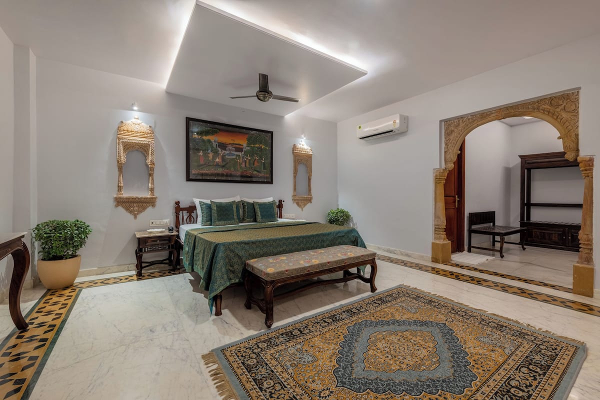 A bedroom with a bed, a bench, a large rug, and decorative wall sconces.