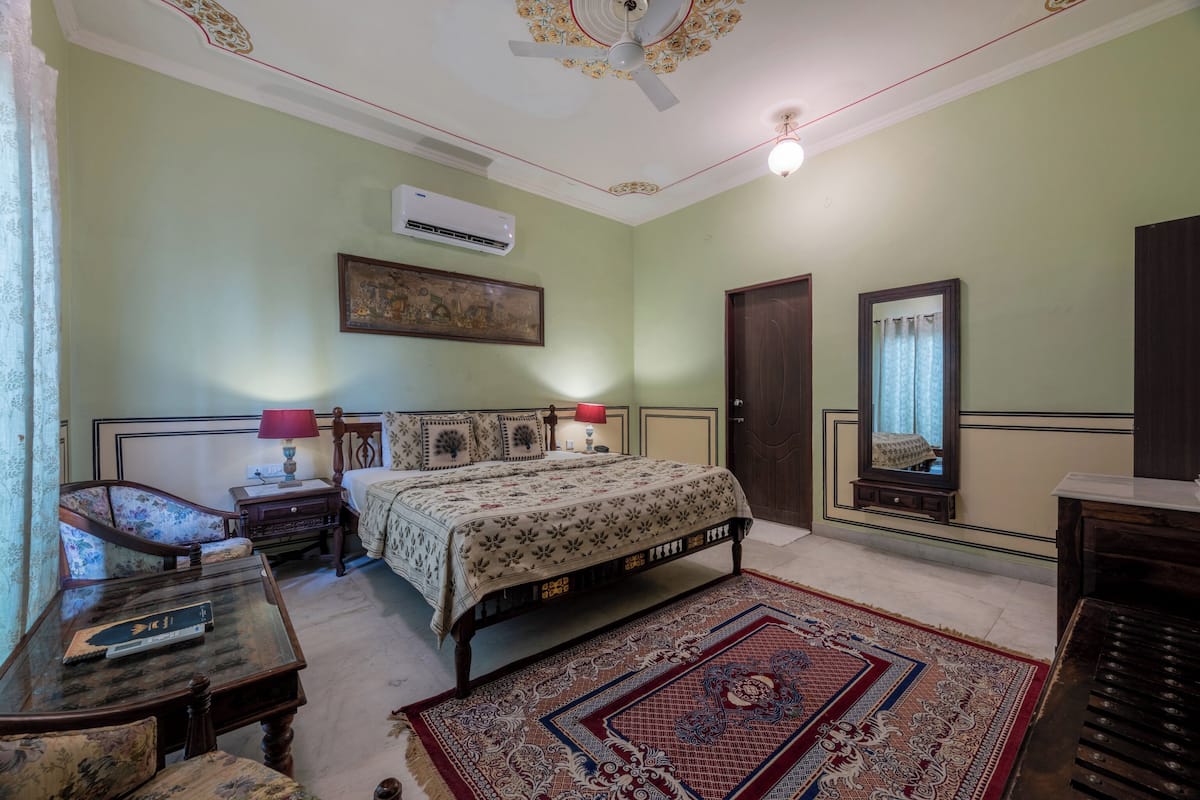 A traditional room with a bed, a desk, a chair, a mirror, and an air conditioning unit.