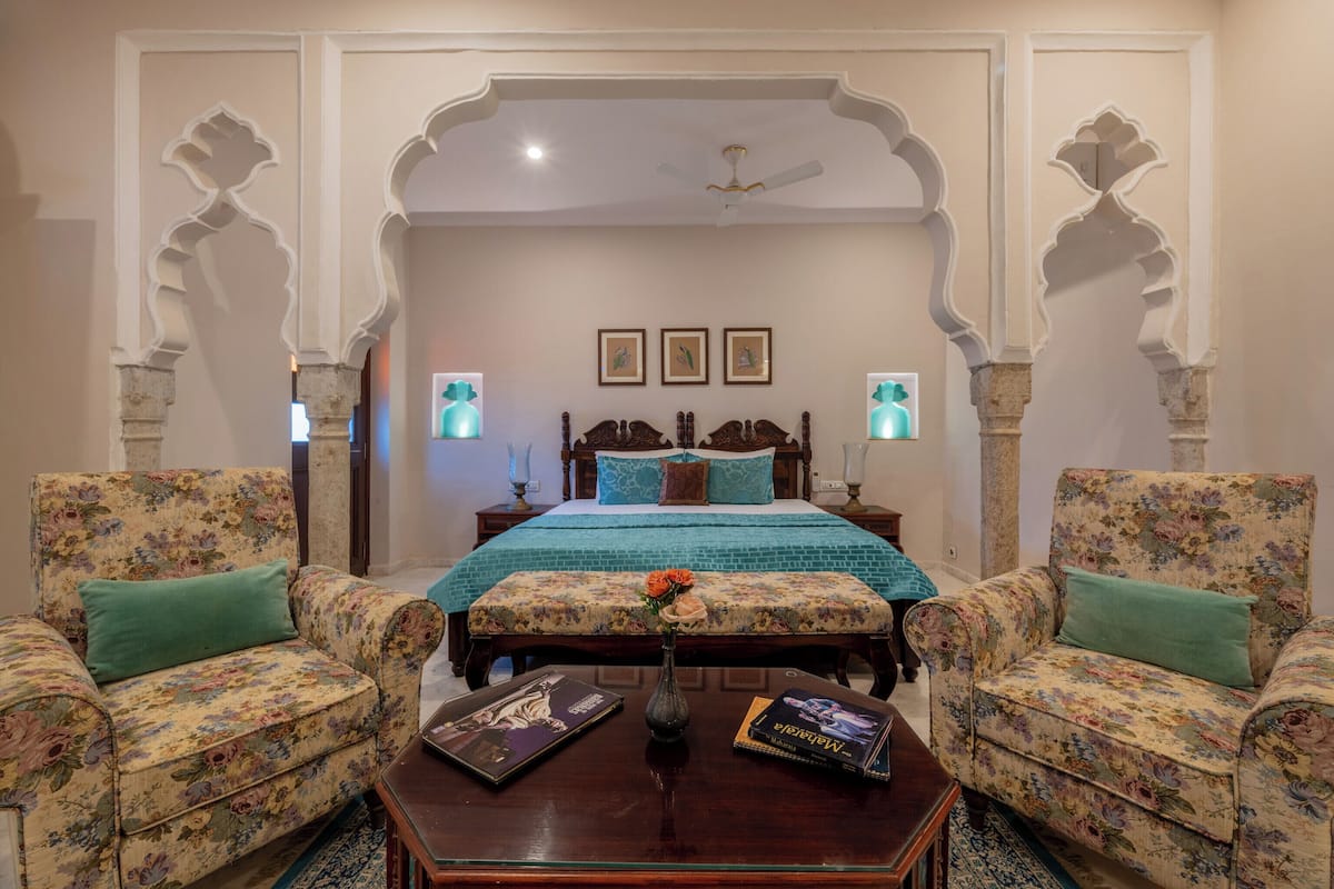 A bedroom with a bed, two armchairs, a coffee table, and a vase with flowers.