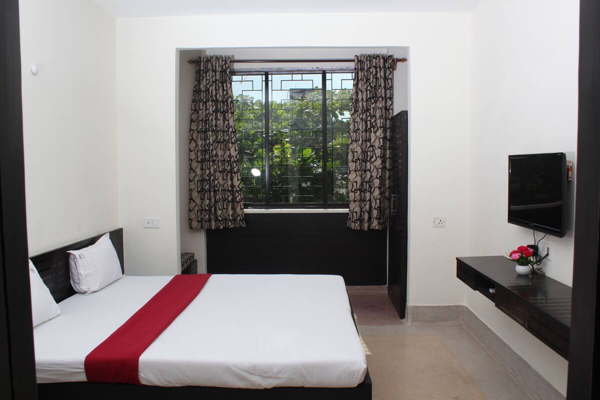 A hotel room with a bed, a TV mounted on the wall, and a window with patterned curtains.