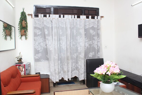 A living room with a red sofa, a black chair, a white vase with flowers, and a television on the wall.