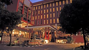 A modern hotel with a red facade, multiple floors, and a covered entrance area. - Merapi Merbabu Hotel Yogyakarta Powered by Archipelago (Depok)