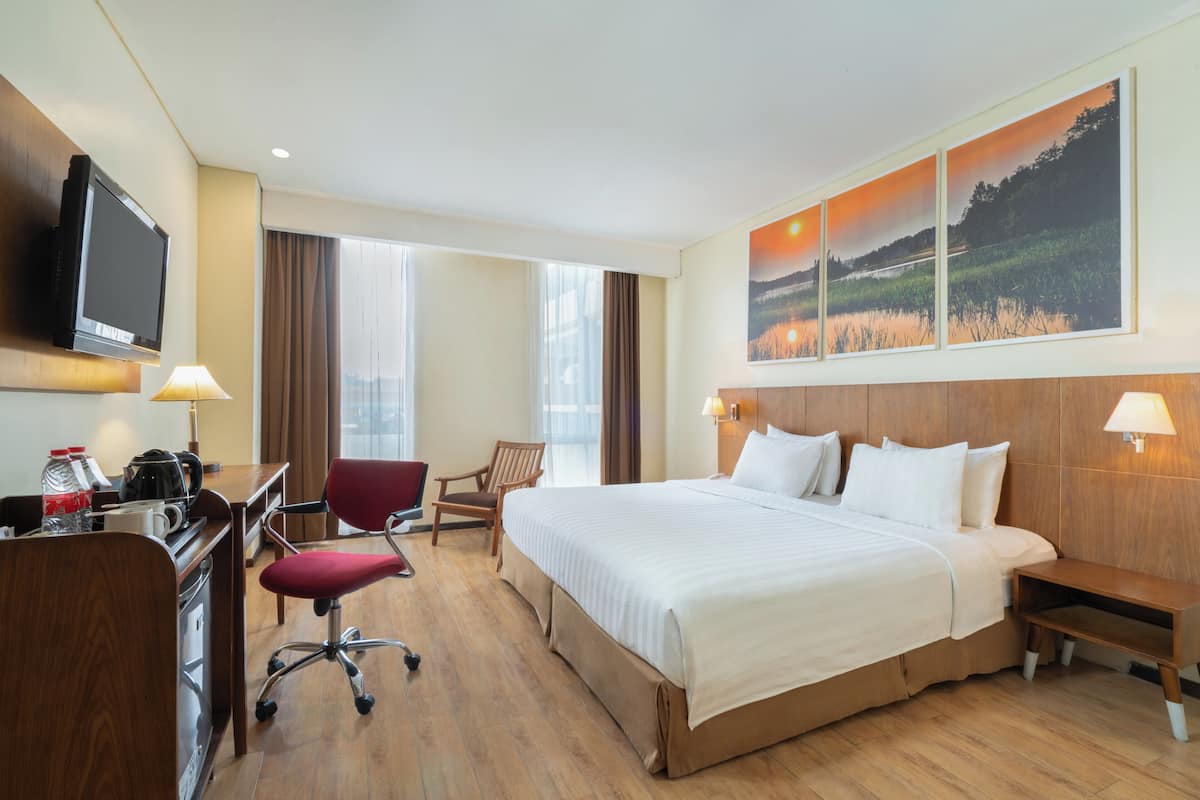 Une chambre d’hôtel avec un grand lit, un bureau avec une télévision, une chaise et un tableau représentant un coucher de soleil.