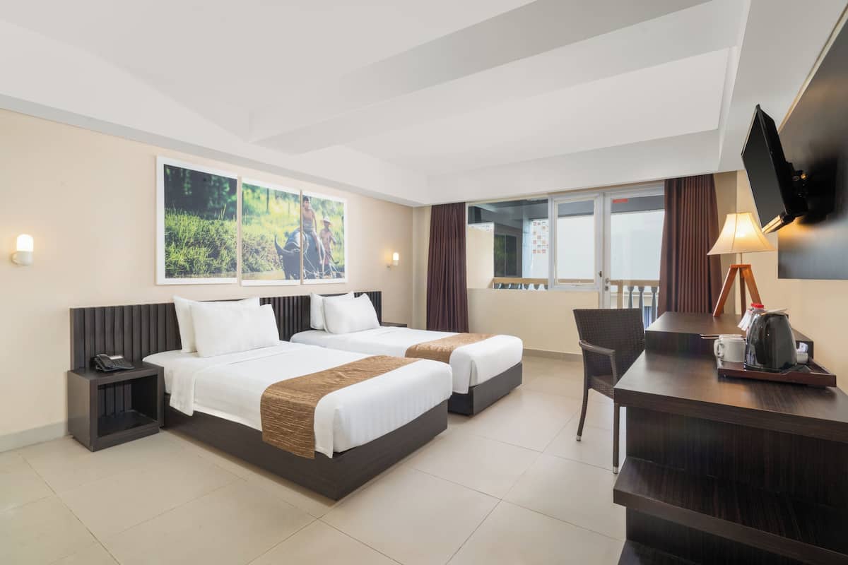 Une chambre d’hôtel avec deux lits, un bureau, une chaise, une télévision et une fenêtre avec des rideaux.
