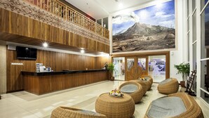 A lobby with a wooden reception desk, wicker seating, a large mural, and a staircase. - Merapi Merbabu Hotel Yogyakarta Powered by Archipelago (Depok)