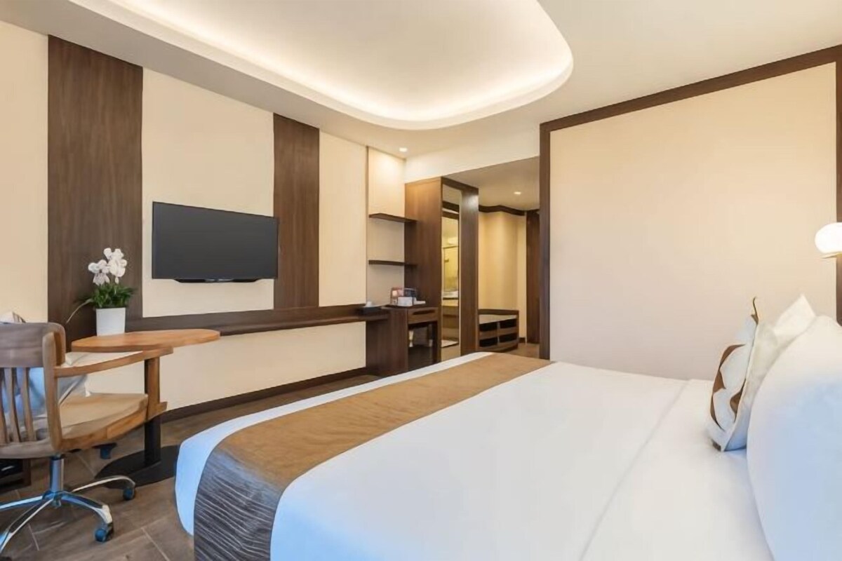 Ett hotellrum med en säng, ett skrivbord, en stol, en tv och ett badrum som syns genom en öppen dörr.