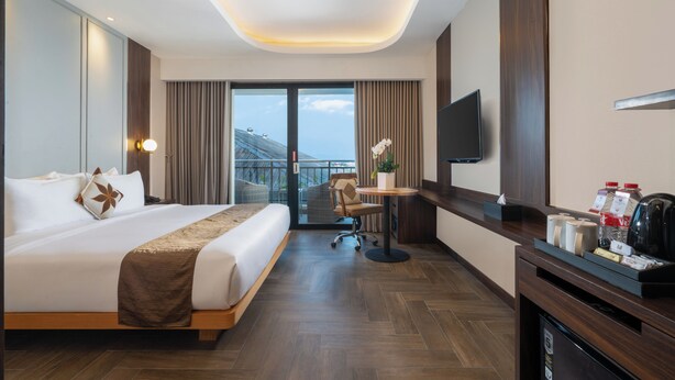 A hotel room with a large bed, a desk, a chair, a television, and a balcony with a view. - Merapi Merbabu Hotel Yogyakarta Powered by Archipelago (Depok)