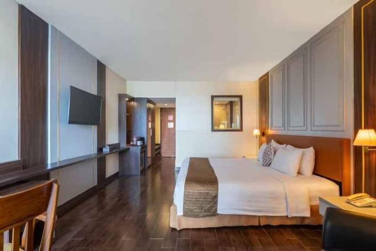 Une chambre d’hôtel avec un grand lit, un téléviseur fixé au mur, un bureau avec une lampe et un plancher en bois.
