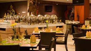 A restaurant with wicker chairs, a buffet with food and drinks, and a statue in the background. - Merapi Merbabu Hotel Yogyakarta Powered by Archipelago (Depok)