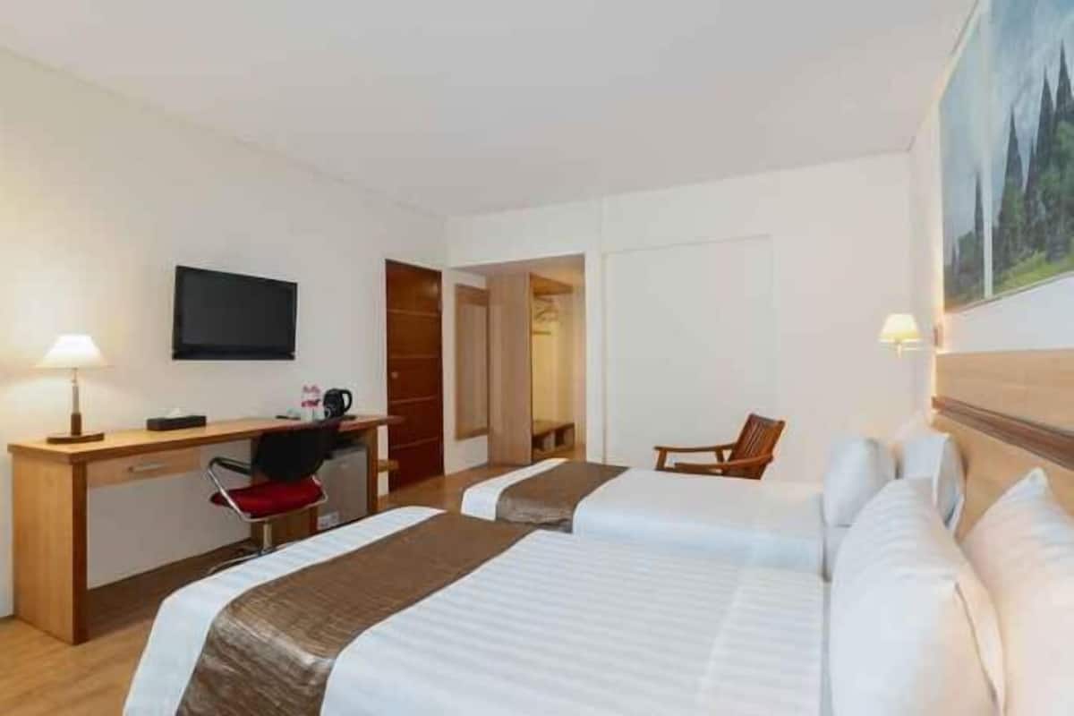 Une chambre d’hôtel avec deux lits, un bureau avec une chaise, une télévision et un tableau au mur.