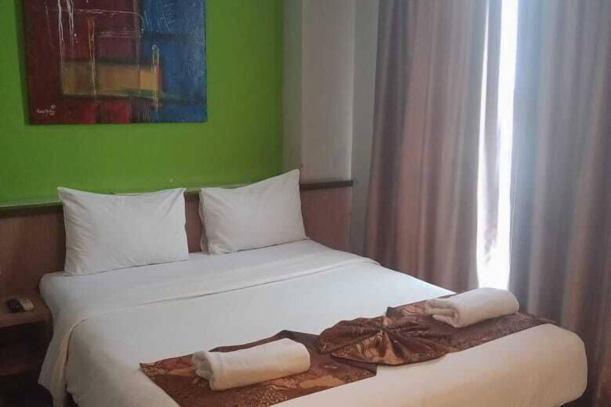 Una habitació d'hotel amb un llit gran, una nit i una pintura a la paret, i una finestra amb cortines.