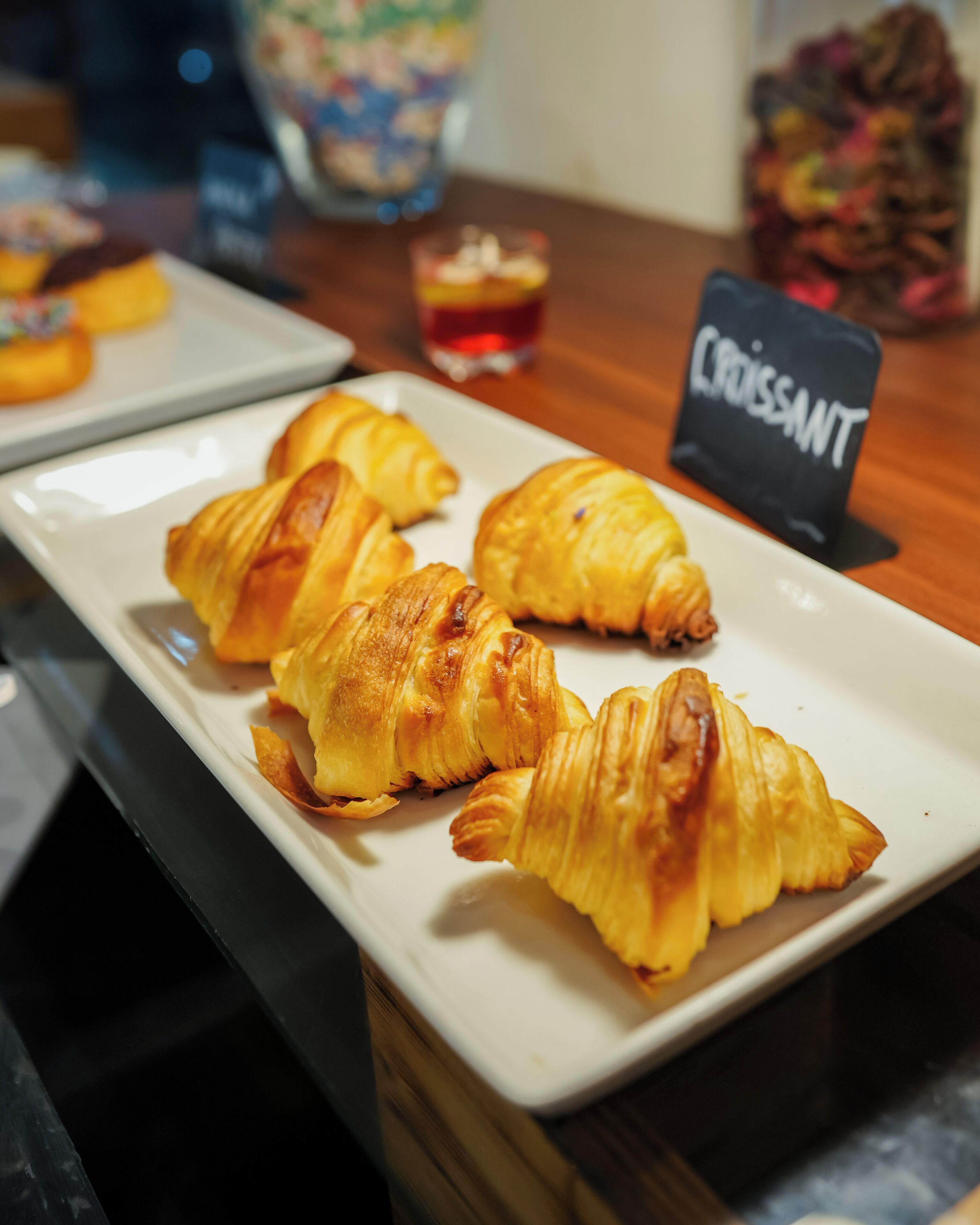 A plate of croissants on a table with a sign labeled 'Croissant' in the background.