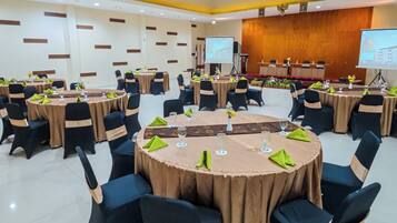 Una sala de conferencias con mesas redondas, sillas negras y un escenario con una pantalla.