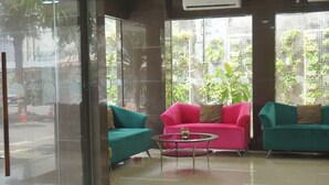 Un hall d’entrée avec des murs en verre, un canapé turquoise, un canapé rose et une petite table ronde.
